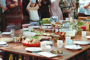 Stół zastawiony potrawami, w tle ludzie trzymający tabliczki.